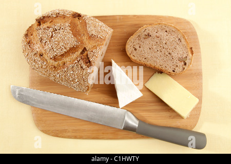 Frisch geschnitzte Getreidespeicher Walnuss-Brot mit zwei Käse Keile platziert auf einer gelben Tischdecke von oben fotografiert. Stockfoto