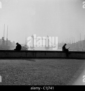 1950er Jahre, zwei Männer sitzen auf einer niedrigen Mauer an der New London Bridge an der Themse auf diesem Foto von J Allan Cash. Tower Bridge in der Ferne. Stockfoto