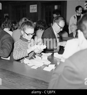 1964, männliche und weibliche Wahlbeamte, die Stimmzettel in einer Wahlhalle während einer politischen Wahl in St Pancras North, London, England, UK, überprüfen. Stockfoto