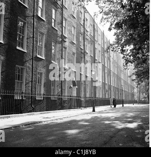 1950er Jahre, historisch, ein Paar, das in einer leeren Straße mit großen fünfstöckigen georgianischen Reihenhäusern steht, London, England, Großbritannien. Stockfoto