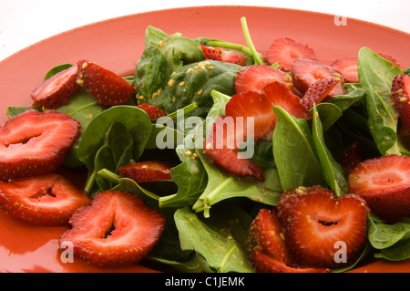 Diese Nahaufnahme ist ein frischer Spinat und Erdbeer-Salat auf einer roten Platte. Hat auch Sesam und Knoblauch für eine köstliche Seite. Stockfoto