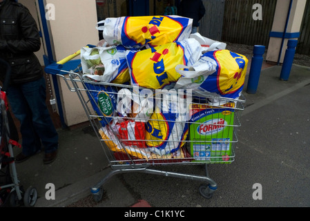 Lidl Supermarkt-Einkaufswagen überlastet mit Plastikträger-Einkaufstaschen voller Lebensmittel außerhalb des Ladens in Großbritannien, KATHY DEWITT Stockfoto