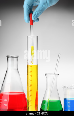 Hand, die Pipette mit aufstrebenden Tropfen Flüssigkeit über Messzylinder. Stockfoto