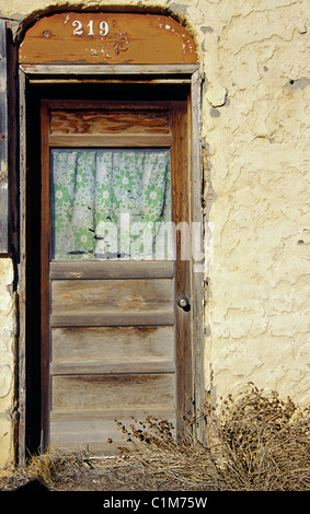 Ein zerrissener Vorhang hängt im Fenster einer alten Holztür in Mountainair, New Mexico gefunden. Stockfoto