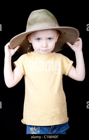 Ein junges Mädchen mit einem Dschungel Stil Safari Hut auf. Ihre Hände sind auf den Hut, und sie zieht es nach unten. Stockfoto