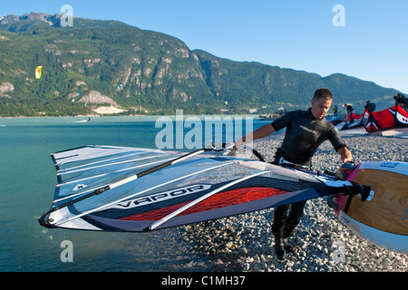 Ein Windsurfer trägt sein Board aus dem Wasser am Ende des Tages. Stockfoto