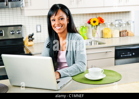 Lächelnde schwarze Frau mit Computer in modernen Küche Interieur Stockfoto