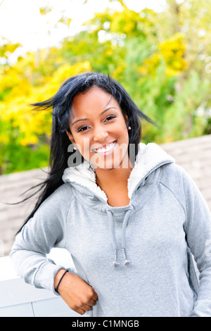 Lächelnde junge schwarze Frau außerhalb in casual Hoodie an windigen Tag Stockfoto