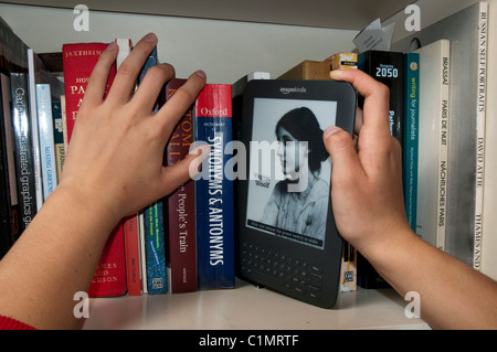 Ein Kindle Model 3 eBook Reader, der in einem Bücherregal in herkömmliche gedruckte Bücher eingefügt wird Stockfoto