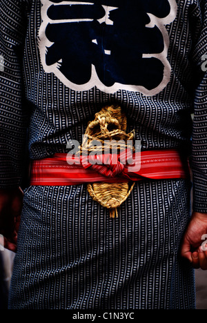 Ein japanischer Mann trägt einen traditionellen blauen Yukata Kimono mit einem roten Obi, Stroh Sandalen (Zori) versteckt in seinem Gürtel. Stockfoto