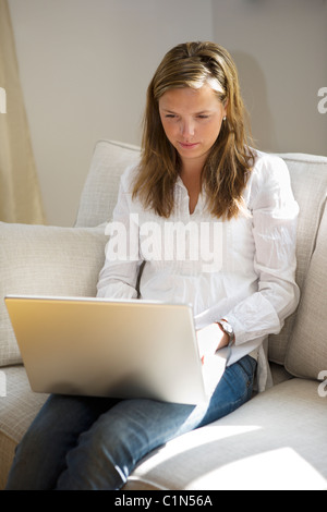 Junge Frau sitzt auf dem Sofa mit laptop Stockfoto