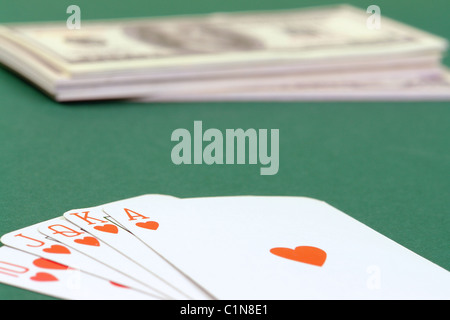 Royal Flush-Karten setzen auf grüne Tischdecke mit Haufen von Dollar im Hintergrund Stockfoto