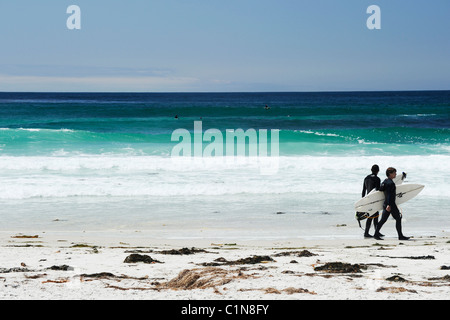 Zwei Surfer in nassen Badesachen am Strand entlang mit ihren Brettern mit Surfer in der Ferne paddeln raus, USA Stockfoto