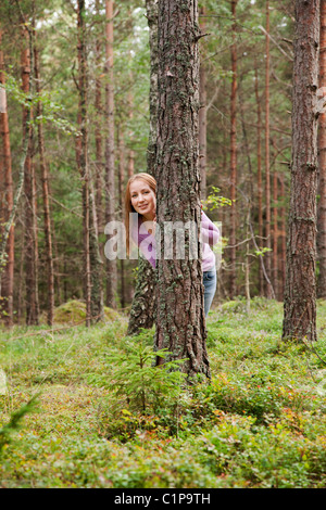 Junge Frau versteckt sich hinter einem Baum im Wald Stockfoto