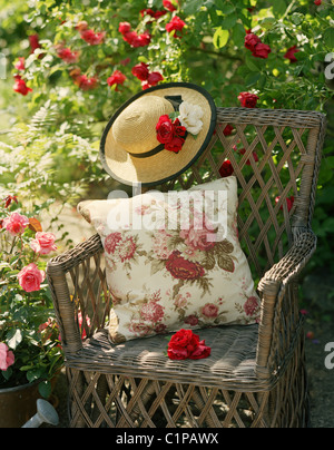 Garten Korbstuhl mit Kissen und Strohhut, umgeben von Rosen Stockfoto