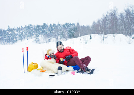 Vater und Tochter trinken aus der Flasche in Winterlandschaft Stockfoto