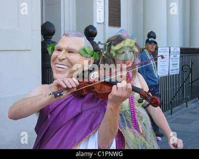 Ein männlicher Entertainer Geigenspiel während in lila Toga gekleidet und trägt eine Maske der US-Präsident George Bush während t Stockfoto