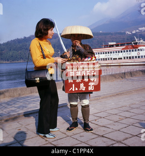 Bild von J Allan Cash eines weiblichen Touristen kaufen eine Vogel-Pfeife von einem Souvenir-Verkäufer an einem See, Japan, 1970er Jahre. Stockfoto