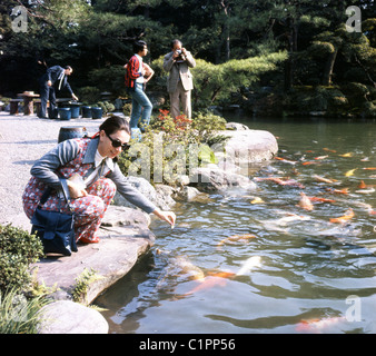 Bild aus den 1970er Jahren durch J Allan Cash.  Frau mit Sonnenbrille und karierte Hose-Anzug füttert die Fische in einem japanischen Steingarten. Stockfoto