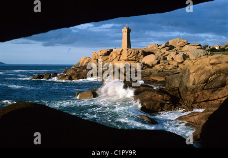 Blick durch Felsen zum Leuchtturm über stürmische See an der rosa Granit Küste. Stockfoto