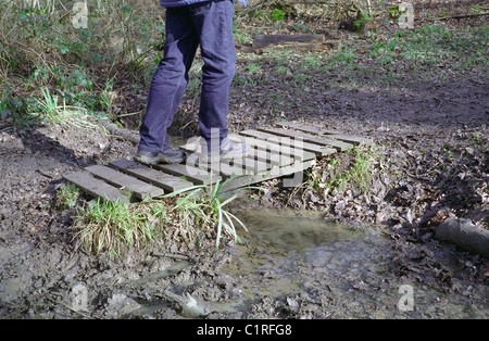 Mann zu Fuß über einen kleinen Holzsteg über einen Bach, UK-Modell veröffentlicht Stockfoto