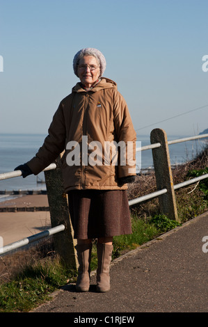Eine ältere Frau posiert für ein Porträt bei einem Spaziergang über den Klippen am Overstrand, Norfolk. Stockfoto