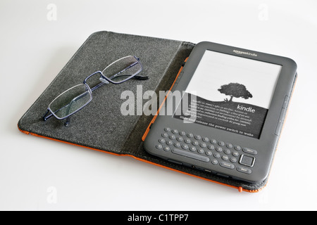 Ein Amazon Kindle Ereader in einem Lederetui mit ein paar blauen halben Felge Lesebrille gegen blass grau hinterlegt. Stockfoto