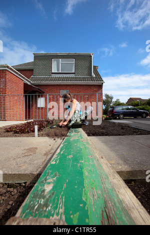 Junge Dame arbeiten und Saat in ihrem Gemüsegarten, sitzend auf einem alten Holzbrett an einem sonnigen Tag Stockfoto