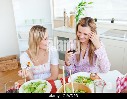 Zwei Frauen in der Küche plaudern und essen Salat mit Gläser Rotwein Stockfoto