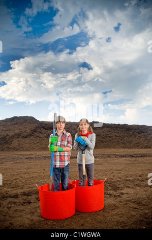 Junge und ein Mädchen im Eimer mit einem Berg von Kompost im Hintergrund stehen Stockfoto