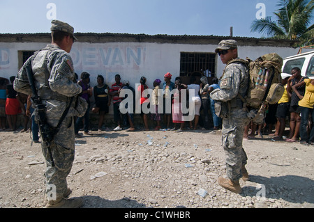 PORT AU PRINCE – HAITI, 15. MÄRZ 2010: US-Marine-Soldaten stehen auf der Wache, während die Einheimischen während der Verteilung von Nahrungsmitteln in der Innenstadt von Port au Prince anstehen, nachdem Haiti am 12. Januar 2010 von einem Erdbeben der Stärke 7,0 heimgesucht wurde Stockfoto