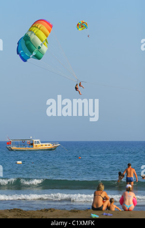 Menschen am Strand entspannen und geschleppt hinter einem Boot auf die bunten Fallschirme. Meer Sarigerme, Ägäis, Türkei Stockfoto