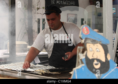 Ein Portugiese grills Sardinen über einem Holzkohlefeuer vor einem Restaurant auf der Straße in Alvor. Algarve PORTUGAL Stockfoto