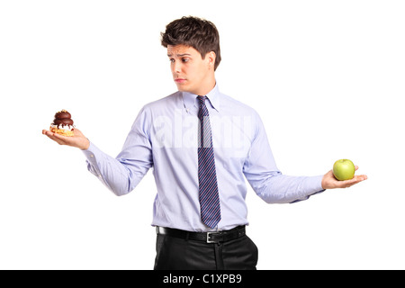 Ein Mann hält einen Apfel und ein Stück Kuchen versuchen entscheiden, welche zu essen Stockfoto