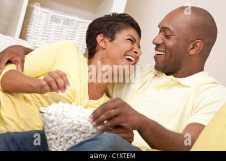 Ein glückliches afroamerikanische Mann und Frau-Paar in den Dreißigern, lachen, Essen Popcorn und einen Film zu Hause sitzen Stockfoto