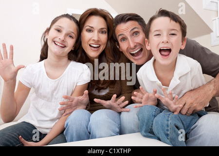 Eine attraktive glückliche, lachende Familie von Mutter, Vater, Sohn und Tochter sitzen auf einem Sofa zu Hause Spaß Stockfoto