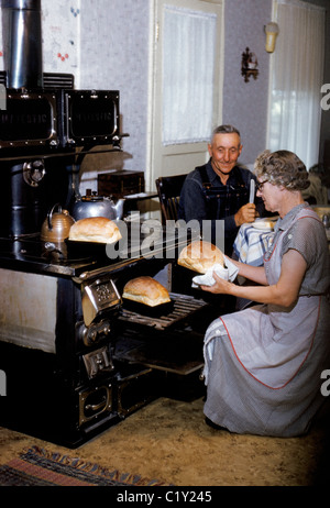 In den 1970er Jahren verwendet eine ältere Frau ihre Vintage Holz-brennenden Koch-Ofen zum Backen von Brot in der Küche ihr altes Bauernhaus in Tremonton, Utah, USA. Stockfoto