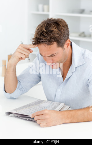 Mann tut eine kryptische Kreuzworträtsel sitzt in seiner Küche konzentriert Stockfoto