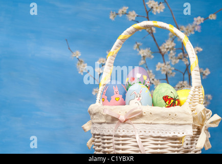 Bunte Osterkorb gefüllt mit handbemalten Eiern, mit Frühlingszweige auf blauem Hintergrund Stockfoto