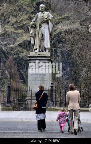 Ein paar mit einem Kind kreuzt Princes Street in Edinburgh, während eine Statue von Thomas Guthrie (1803 – 1873) schaut. Stockfoto