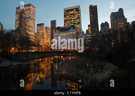 New York City-Blick auf das Plaza Hotel und andere Türme mit Reflexionen in den Teich von Gapstow Brücke im Central Park gesehen. Stockfoto