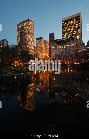 New York City-Blick auf das Plaza Hotel und andere Türme mit Reflexionen in den Teich von Gapstow Brücke im Central Park gesehen. Stockfoto