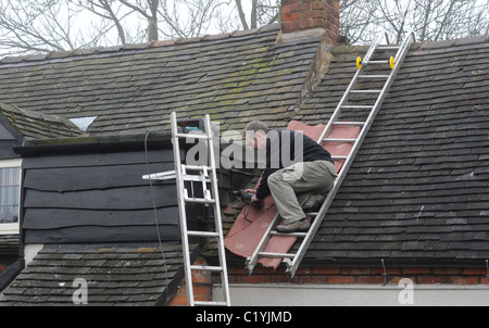 ARBEITER ARBEITEN AUF DACHLEITERN AUF INLÄNDISCHEN HAUS RE DACH REPARATUREN DIGITALUMSTELLUNG NEUE ANTENNEN SIGNAL ANALOGABSCHALTUNG UK Stockfoto