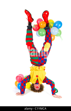 Lustiger Clown mit Luftballons im Kopfstand auf weißem Hintergrund Stockfoto