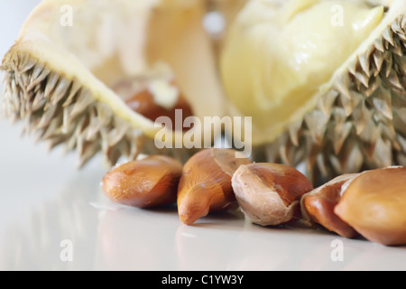 Durian Samen mit Durian Fruchtfleisch und Schale im Hintergrund, mit Reflexionen auf dem Tisch Stockfoto