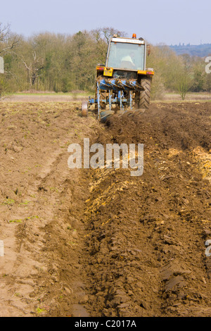 Mann in einem kleinen Traktor ein Feld mit einem Pflug Pflügen. Stockfoto