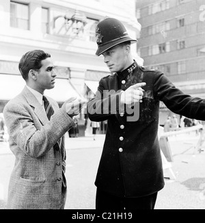 1950s, historisch, London und ein neu eingetroffenen Einwanderer in Großbritannien erhalten Anweisungen von einem britischen Polizisten in der Uniform und Helm der Ära. Stockfoto