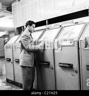 1950s, ein Mann in Anzug und Krawatte, ein neu angekommener Mann, der nach Großbritannien einwanderte und einen Münzautomaten in der Londoner U-Bahn, England, benutzte. Stockfoto