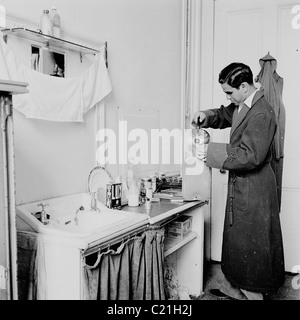1950s, ein neu angekommener Einwanderer aus Übersee in Großbritannien, der am Waschbecken in seinem Bett stand und Wasser aus einem Wasserkocher in eine Heißwasserflasche goss. Stockfoto