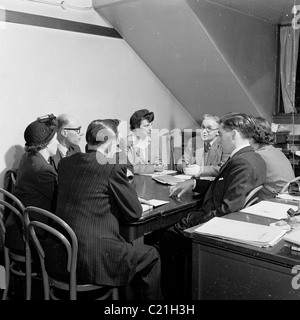 1950er Jahre, England. Kleine Gruppe von Männern und Frauen, die eine geschäftliche Konferenz, sitzen um einen Tisch in einem Manager in diesem historischen Bild. Stockfoto